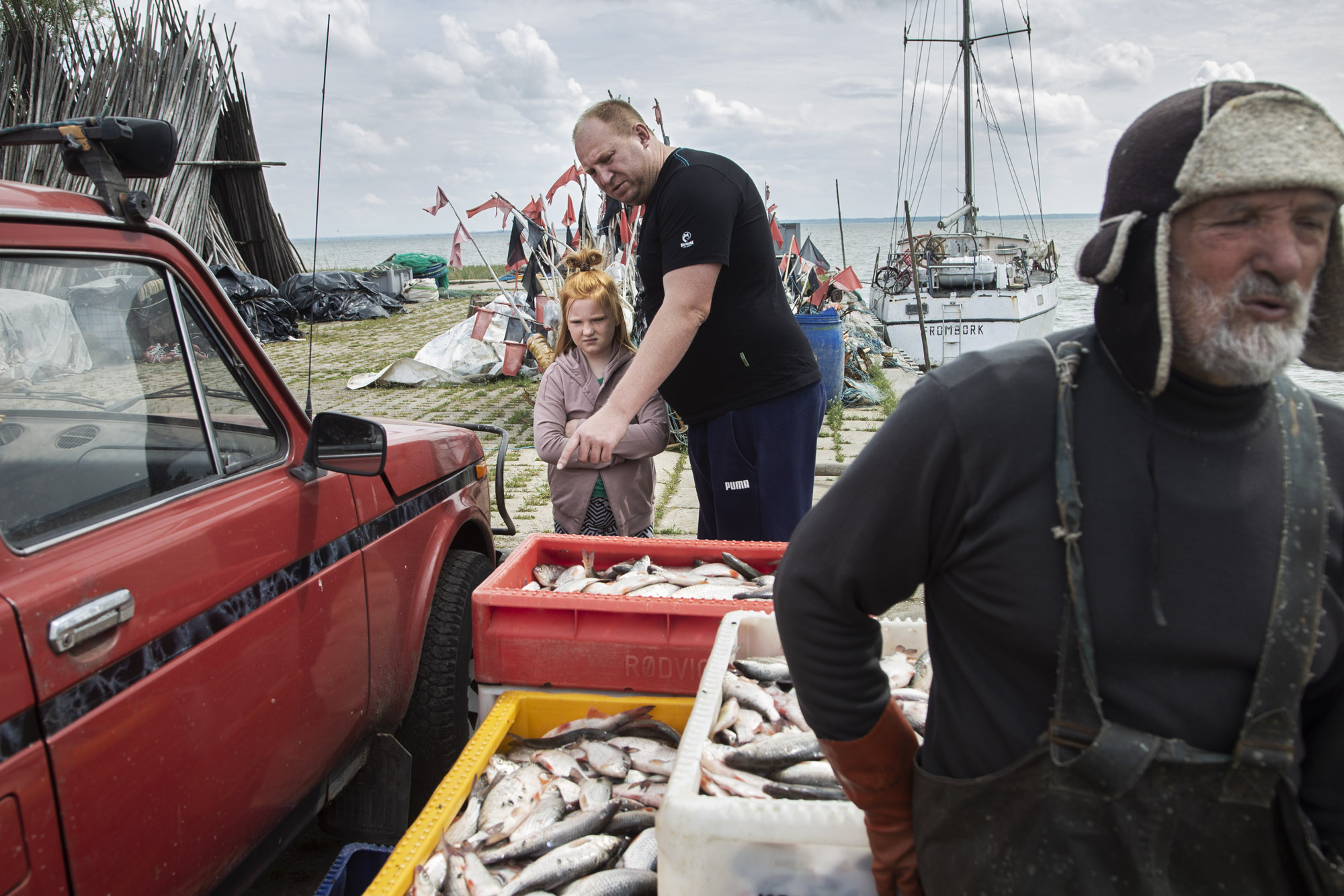 2021.05.16. Port w Piaskach na Mierzei Wislanej. Bracia Waldemar (z prawej) i Krzysztof Gotkowscy po polowie wyladowuja ryby z lodzi. W porcie czeka juz na nich niewielka grupka turystow, ktorzy kupuja ryby &quot;z burty&quot;, czyli bezposrednio do rybakow.  